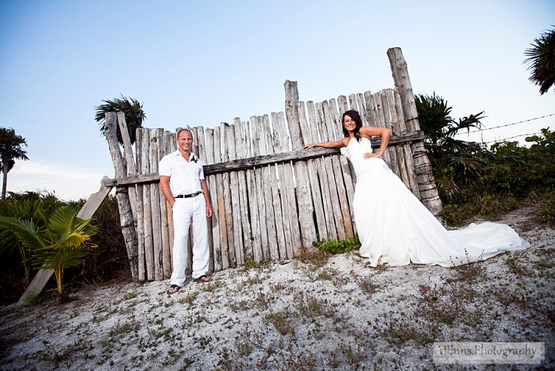 The bride and groom leaning against what left of an old fence