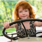 Little Girl with red hair sitting behind the wheel of a tractor