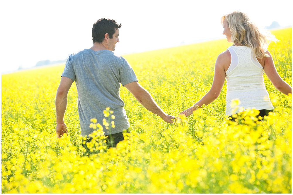 holding hands walking through the canola for engagement photos