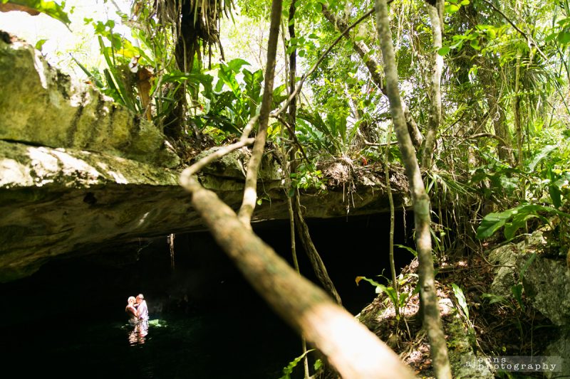 the couple in the water under a massive ledge in a cenote in the mayan.