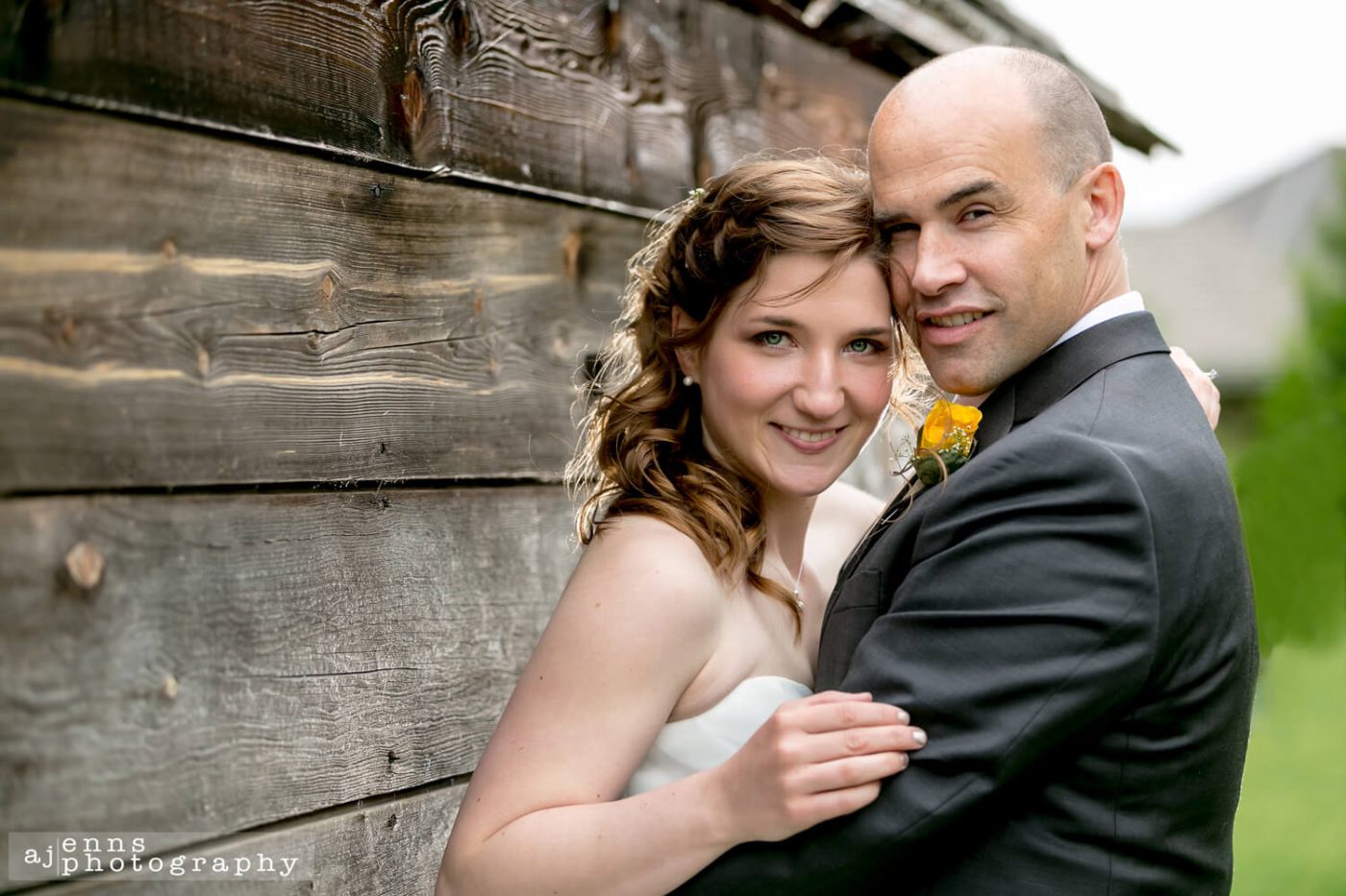 The beautiful bride and groom leaning against a wooden wall