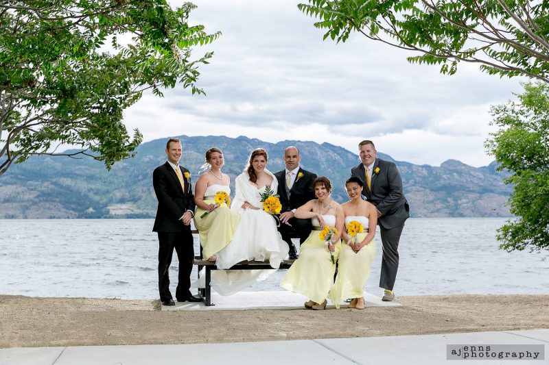 The couple sitting on a picnic table over looking Kelownas lake with the mountains in the background.