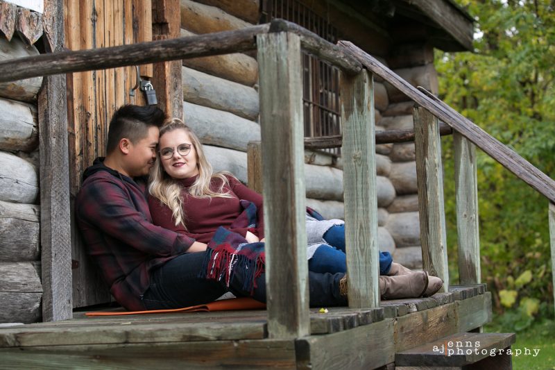 Engagement photos sitting against a log cabin on the steps