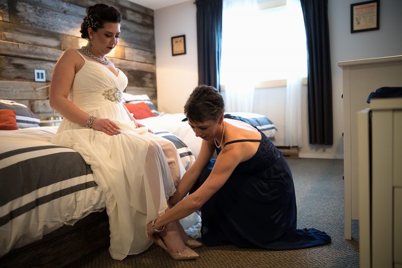 The bride's mother putting on her daughters shoes.