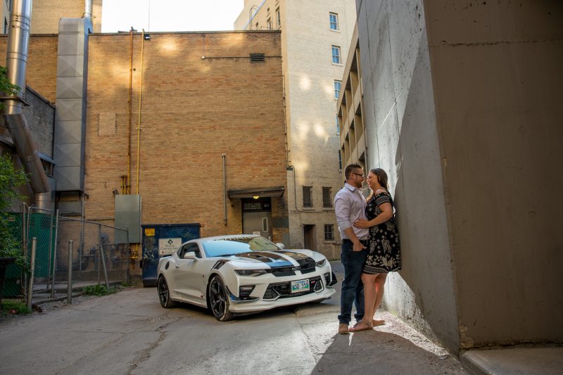 The couple leaning into each in a back alley in front of Kursty's Camaro