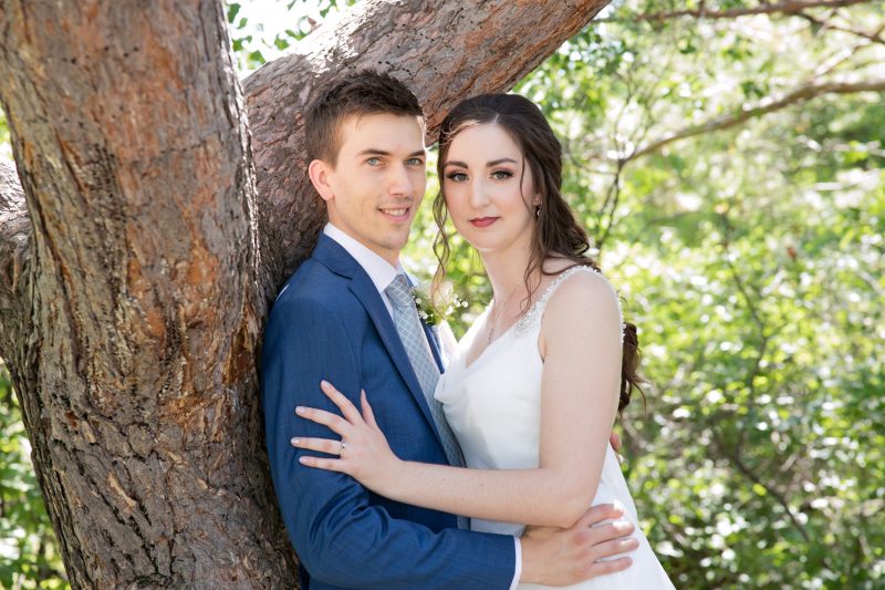 The couple holding each other while leaning against a tree in the shade