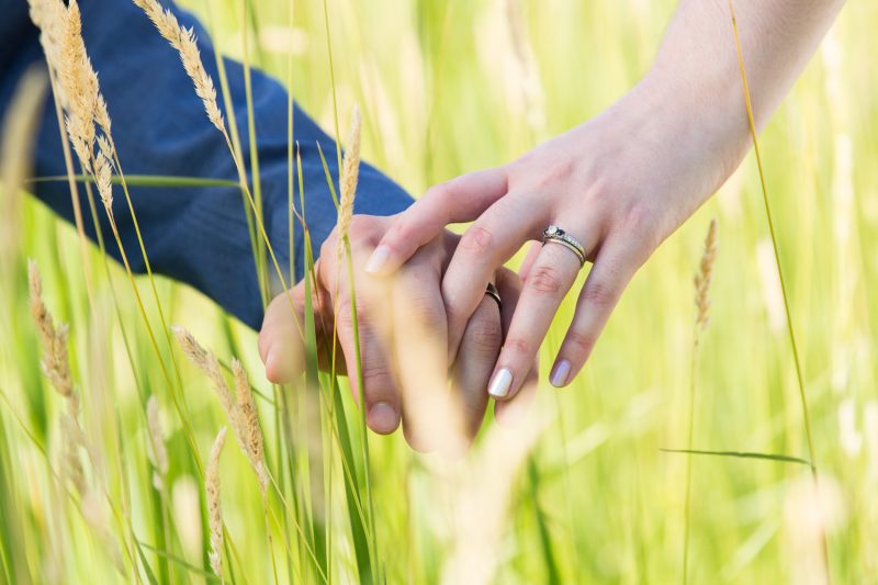 The couple holding hands amongst some large blades of grass.