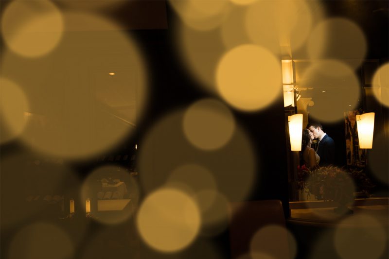 A reflection of the couple kissing with lights out of focus in the foreground.