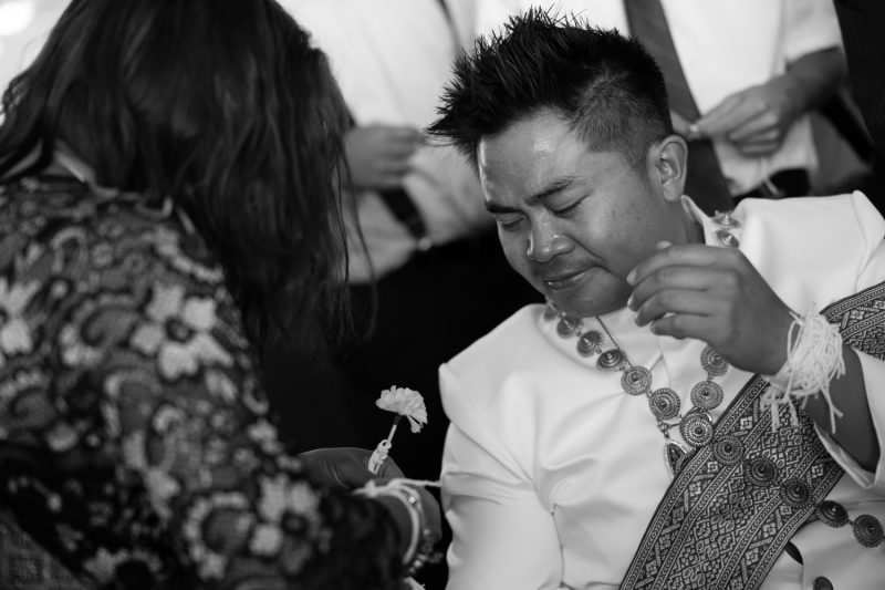 The groom crying while a family member ties the white string on his wrist