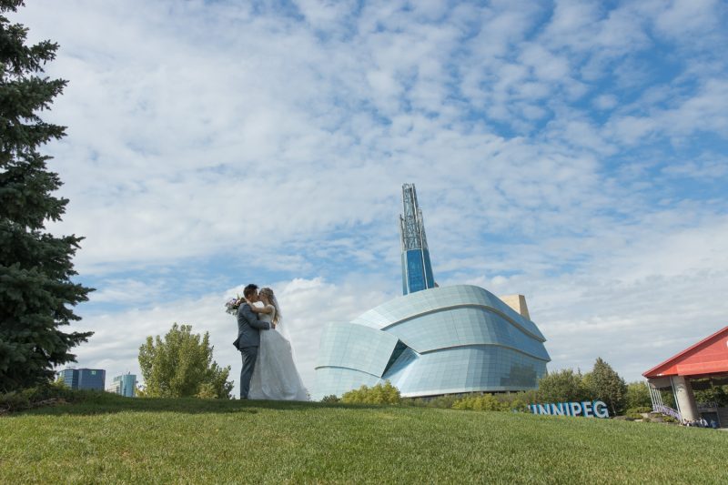 The couple kissing on the top of a hill with the Museum in the background