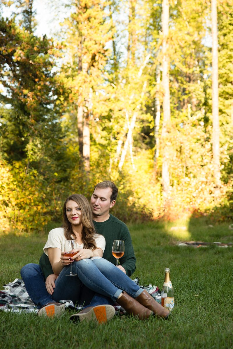 The couple cuddling while sitting on a blanket at sunset holding champagne
