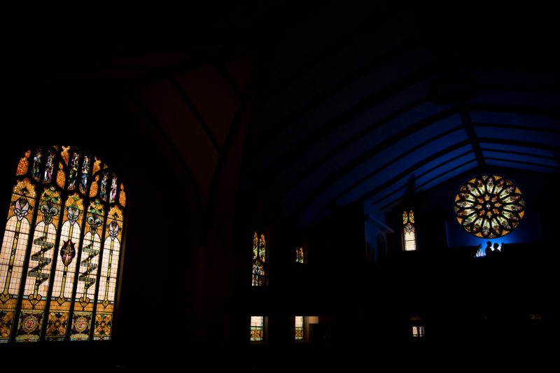 The couple being back lit with blue light and color streaming in through multiple stained glass windows