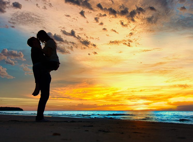 Brendan holding Alrita up on the beach in front of an amazing Sunset