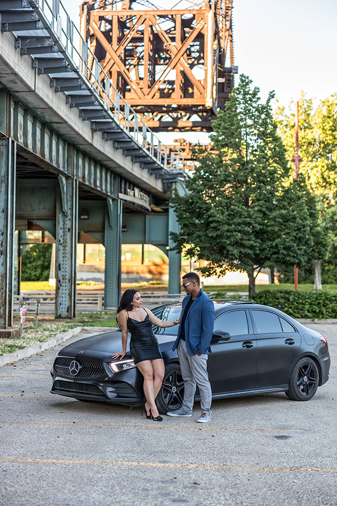 The couple posing with their car under a train bridge
