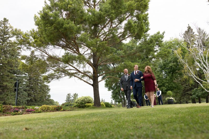 The groom and his parents walking down the grassy isle
