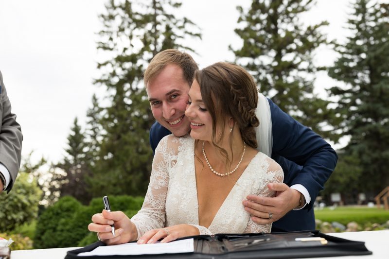 Arlita signing the wedding documents with Brendan leaning over and hugging her