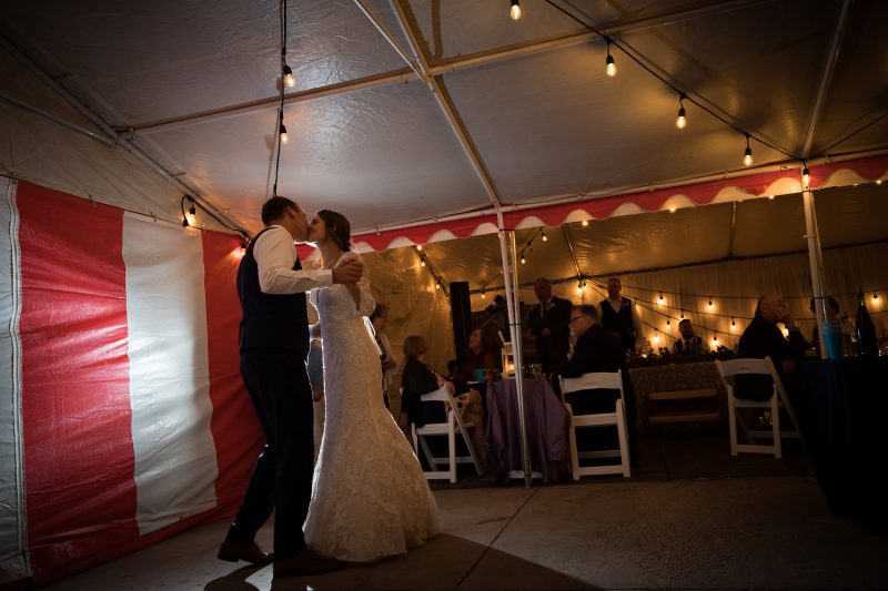 Backlit first kiss under the reception tent