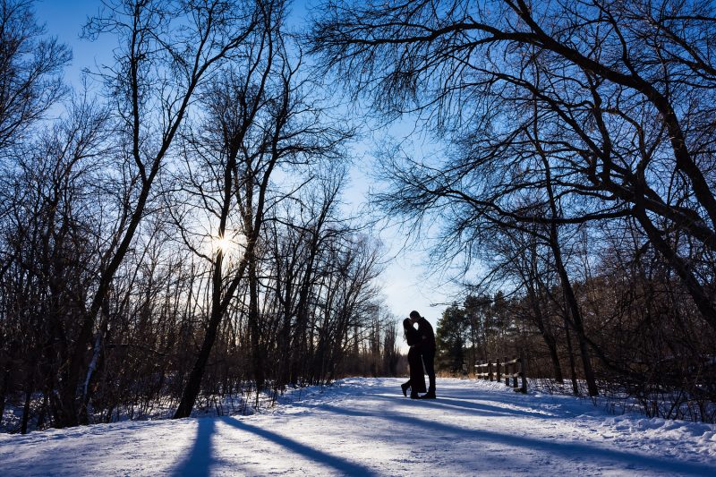 A sillouette of the couple kissing amongst the trees with the sun in the background