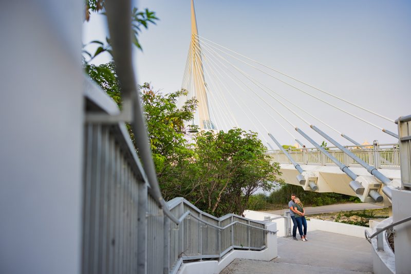 The couple cuddling against a stair handrail with the Esplanade Riel bridge in the background