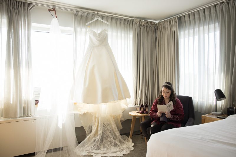 Meaghan reading a card in the corner with her wedding dress hanging from the window