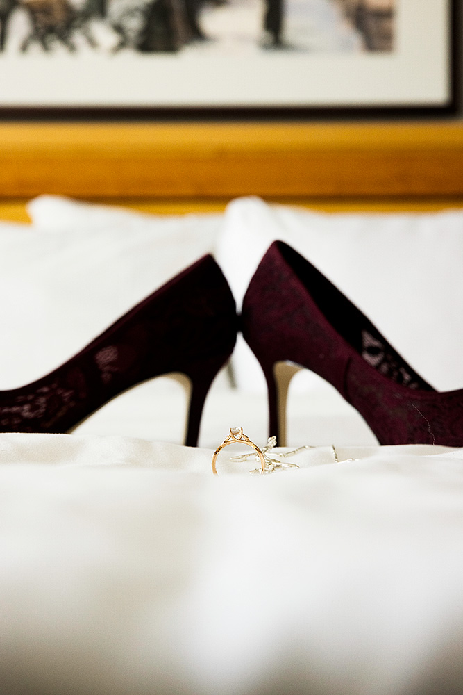 the engagement ring balanced on the white bed sheets with the purple wedding shoes in the background