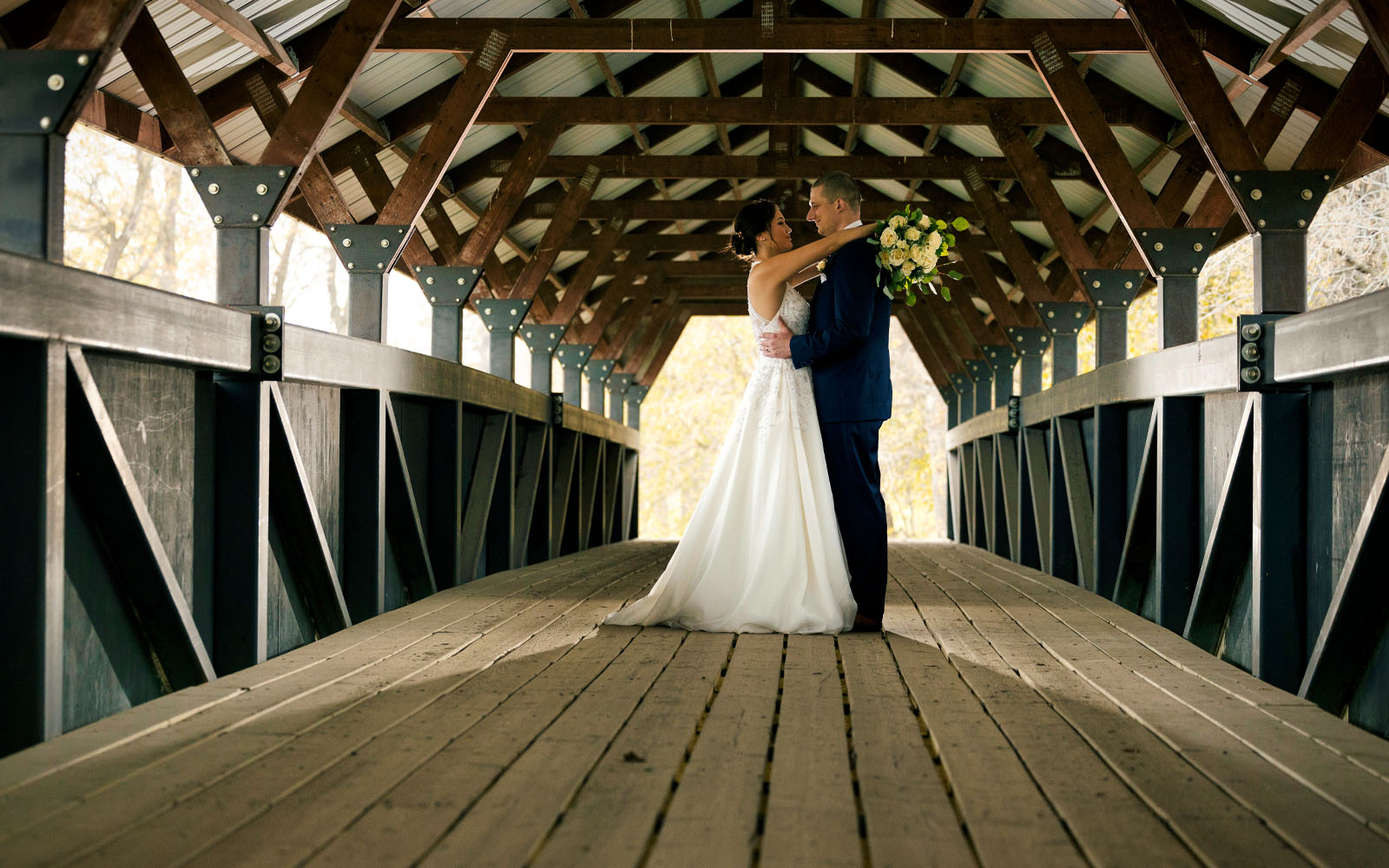 The bride and groom embracing under the canopy of one of the many bridges at Bridges Golf Course