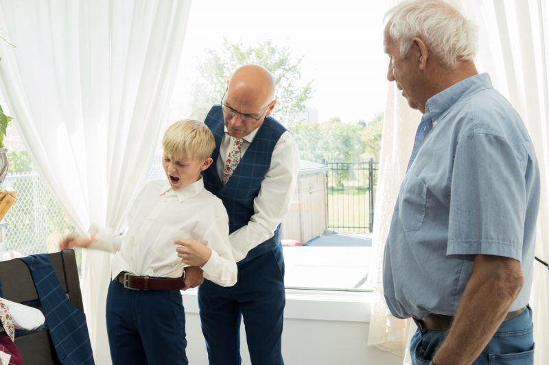 The groom helping his son tuck his shirt in and his son making a funny face