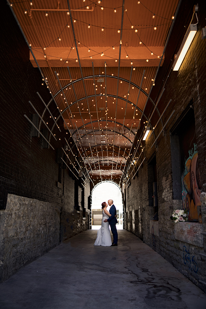 The couple kissing in a dark alley with the entire ceiling lit up with string lights