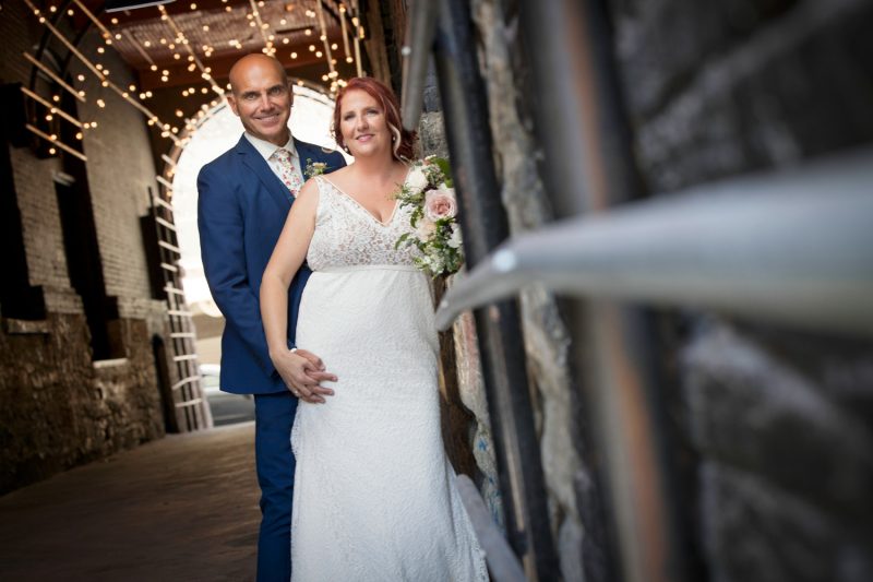 The bride and groom standing in a alley letup with string lights