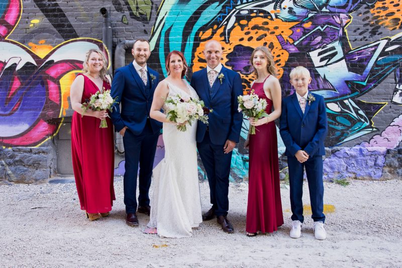 The whole wedding party poses in front of a graffiti wall