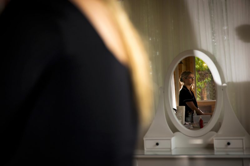 The view of the bride sitting getting her makeup through a mirror with silhouette lighting