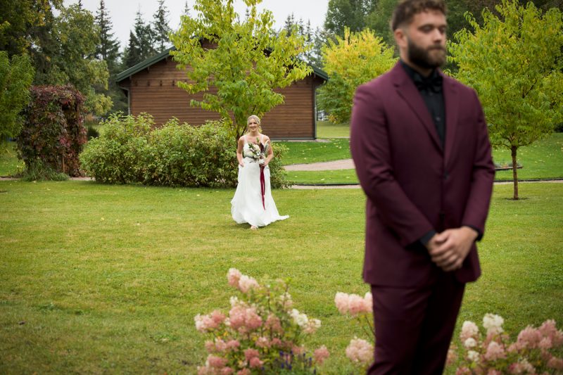 Karlie walking up a grassy field with the groom blurred in the foreground for the first look
