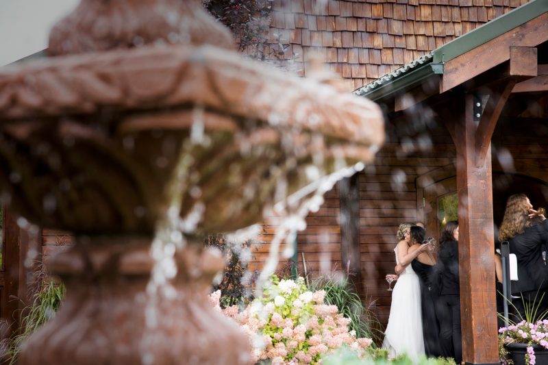 The bride and her sister hugging viewed through water falling from a water fountain