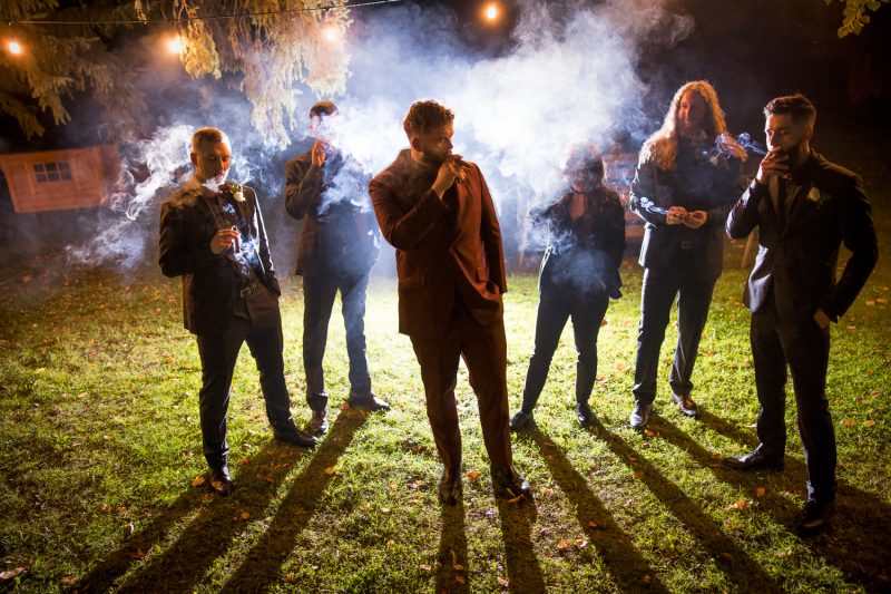 Jeremy and the groomsmen smoking cigars while being back lit at night time.