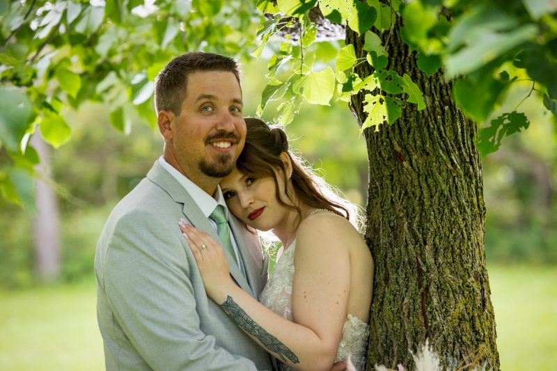 Danielle leaning on Jons chest for a portrait under a tree