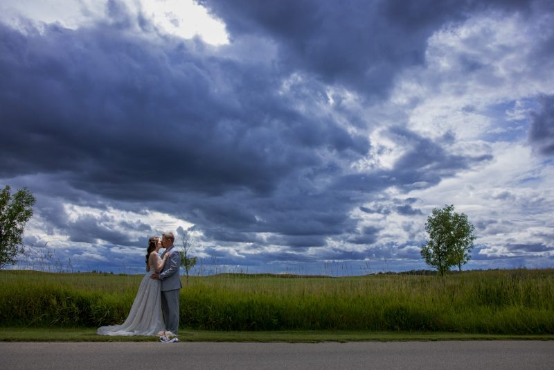 The couple under a ultra moody sky while they embrace with a wheat field in the background