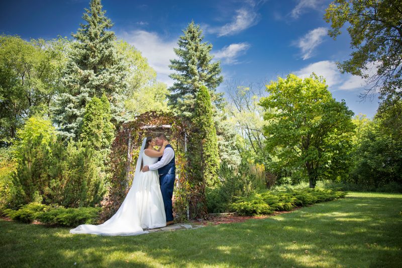 the couple kiss in front of a arbor at Evergreen Village