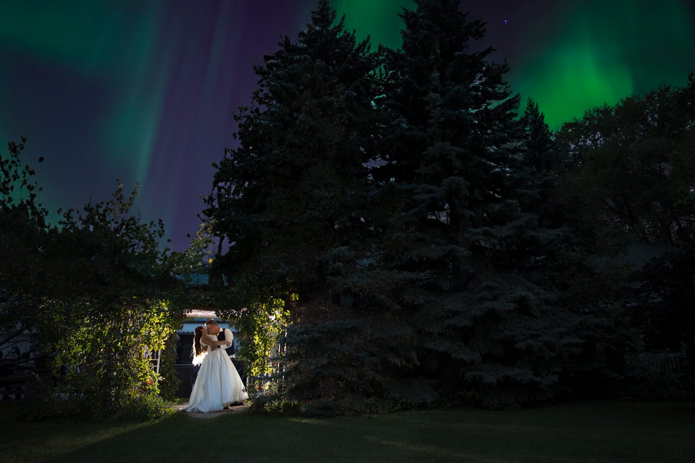 Mike dips Nicky under a arbour being back lit under the sky with dancing northern lights