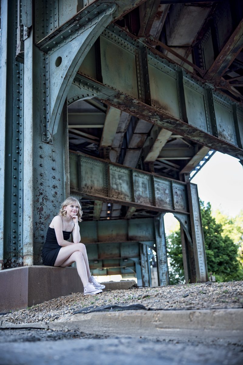 Brooklyn sitting underneath a metal, rusty train bridge