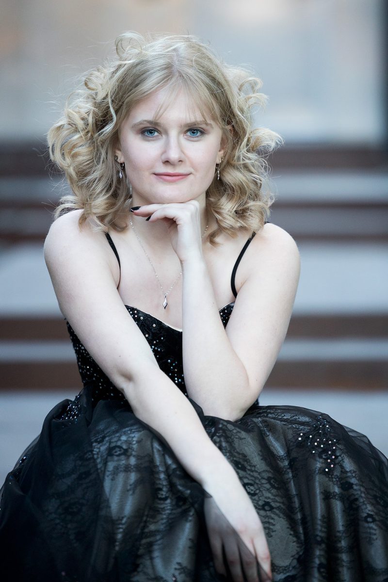 A young woman sitting on stairs in a black dress resting her chin on your hands